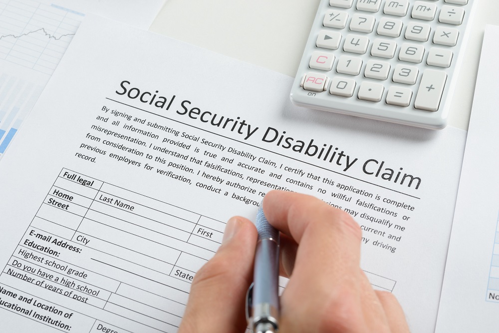 Person’s Hand with Pen Filling Out SSD Form|Black Pen Laying on Top of Worker’s Comp Form